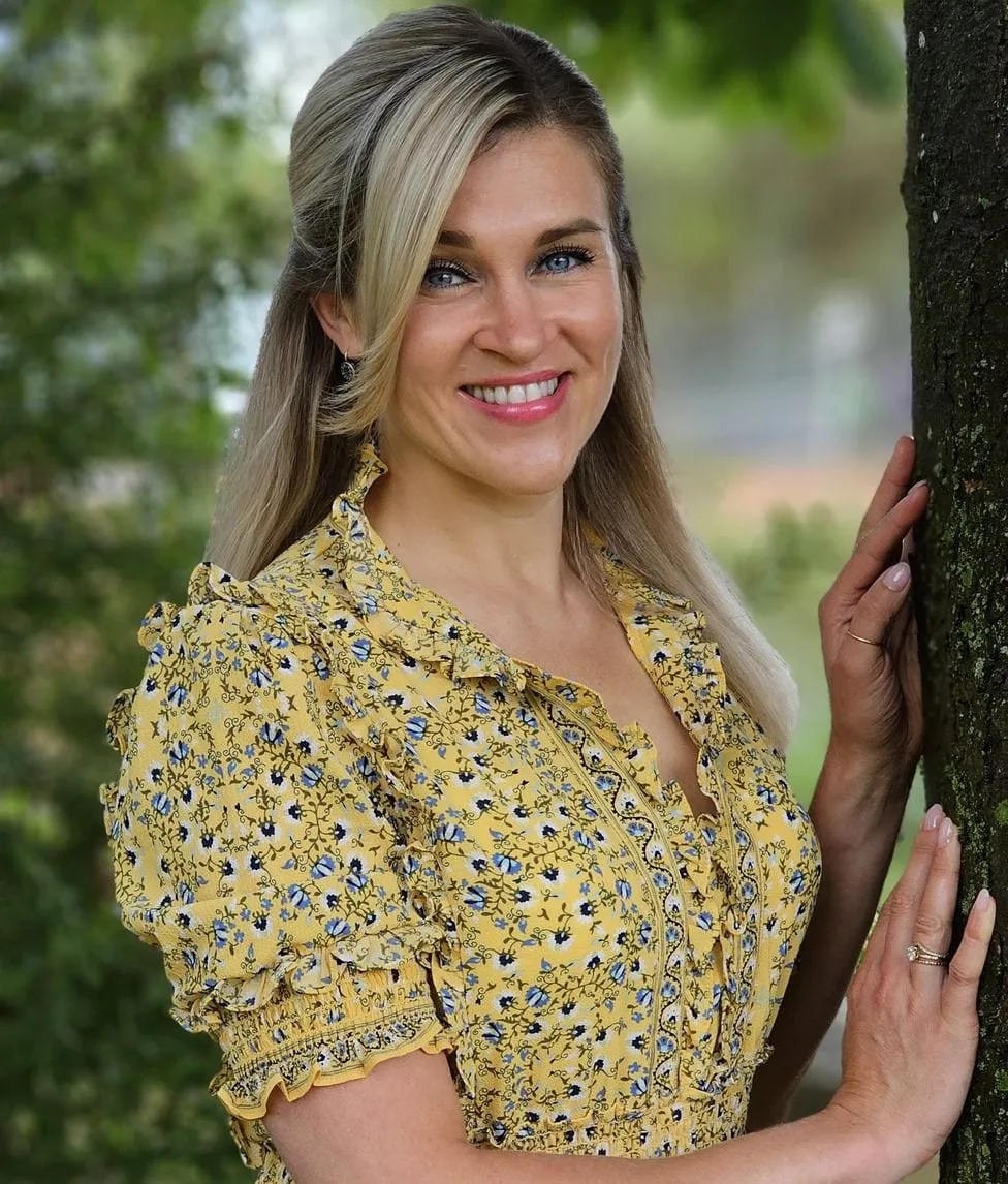Natalie Leer in gelber Bluse an einem Baumstamm, lachend